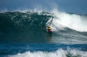 A person kayak surfing a large wave.