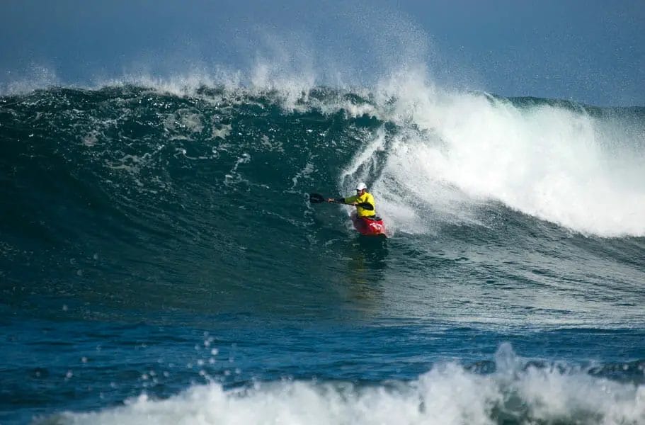 A person kayak surfing a large wave.