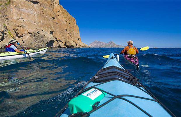Two people kayaking in Mexico near a cliff.