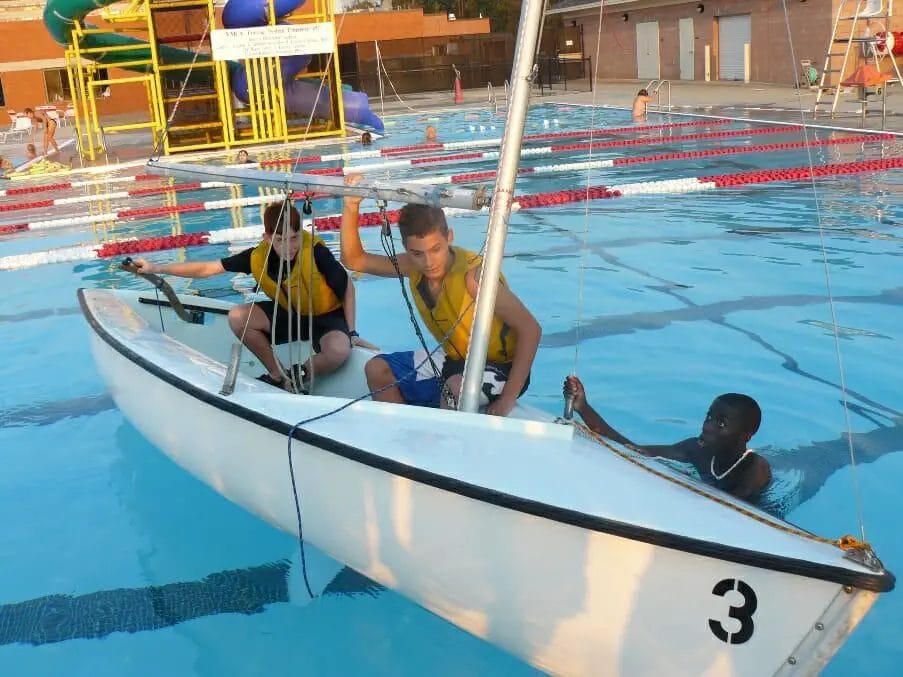 A group of boys in a boat in a pool during a capsize drill.