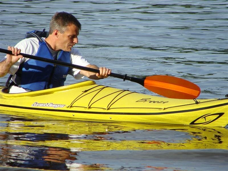 A man is paddling a Current Designs yellow kayak.