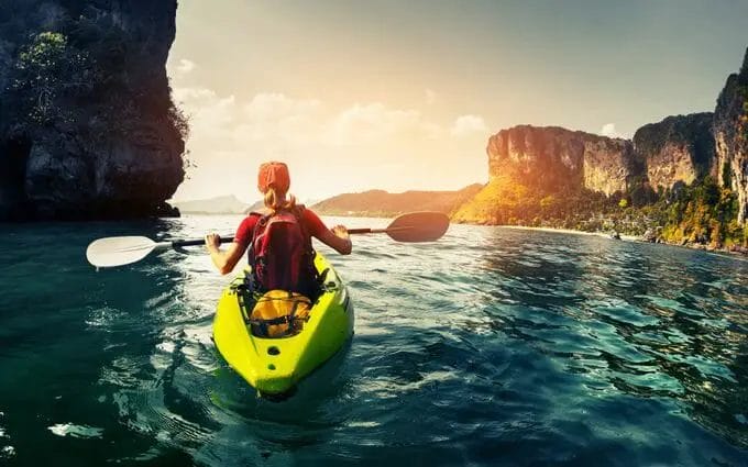 A woman is kayaking in the ocean near cliffs.