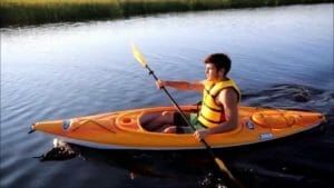 A man is paddling a Pelican kayak on the water.
