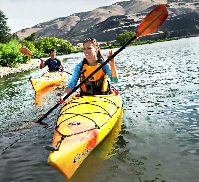 Two people paddling in a yellow Perception Kayak on a river.