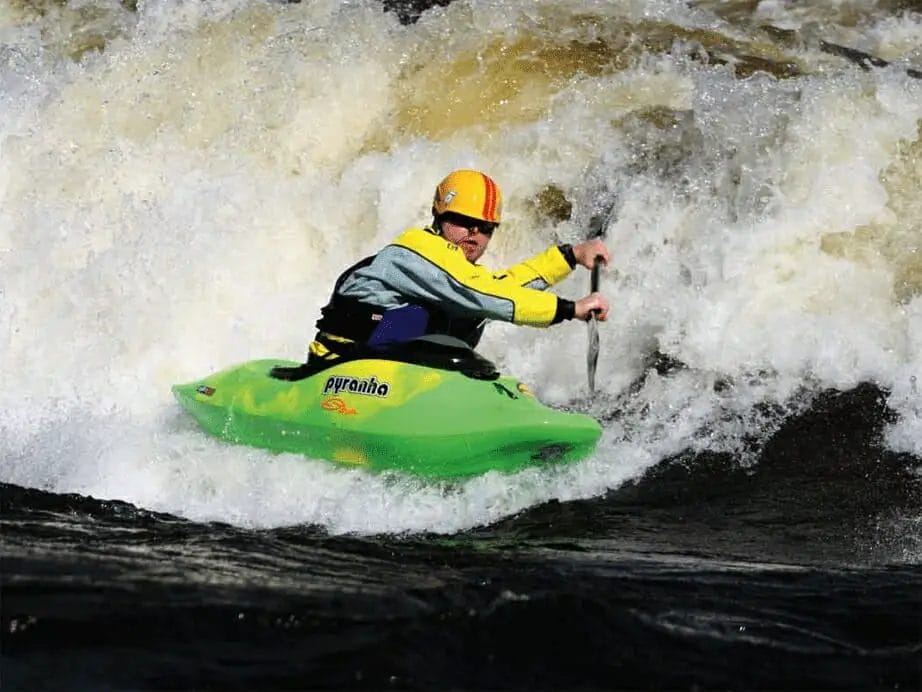 A man in a green Pyranha Kayak on a river.