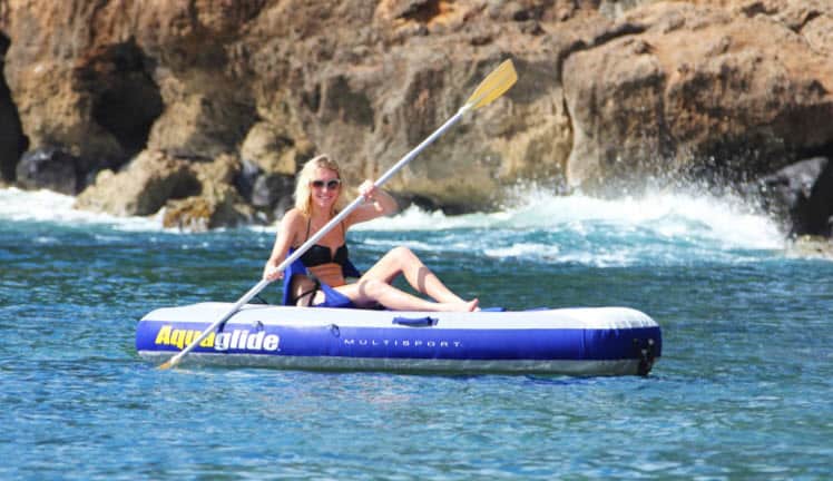 A woman paddles an inflatable raft in the ocean.