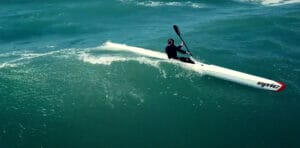 A man riding a surfski kayak on a wave in the ocean.