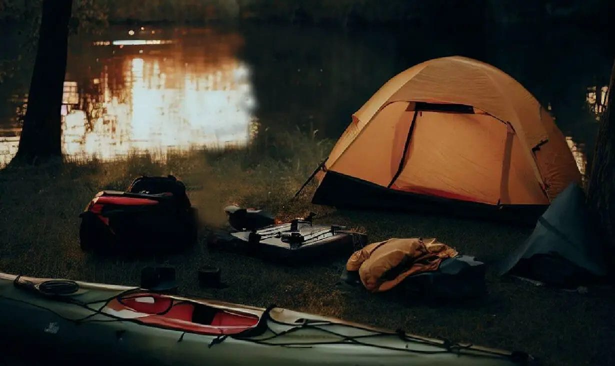 A kayak camping tent set up near a lake with a canoe.