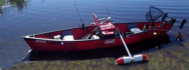 A small red canoe with a fishing pole in the water.