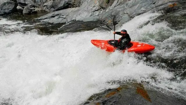 A man is kayaking down a waterfall in a red Dagger Kayaks kayak.