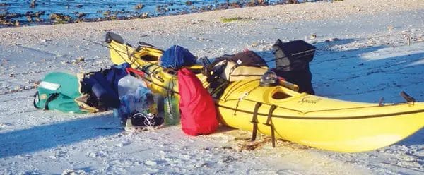 A yellow kayak on the beach, prepared for an overnight kayak trip.