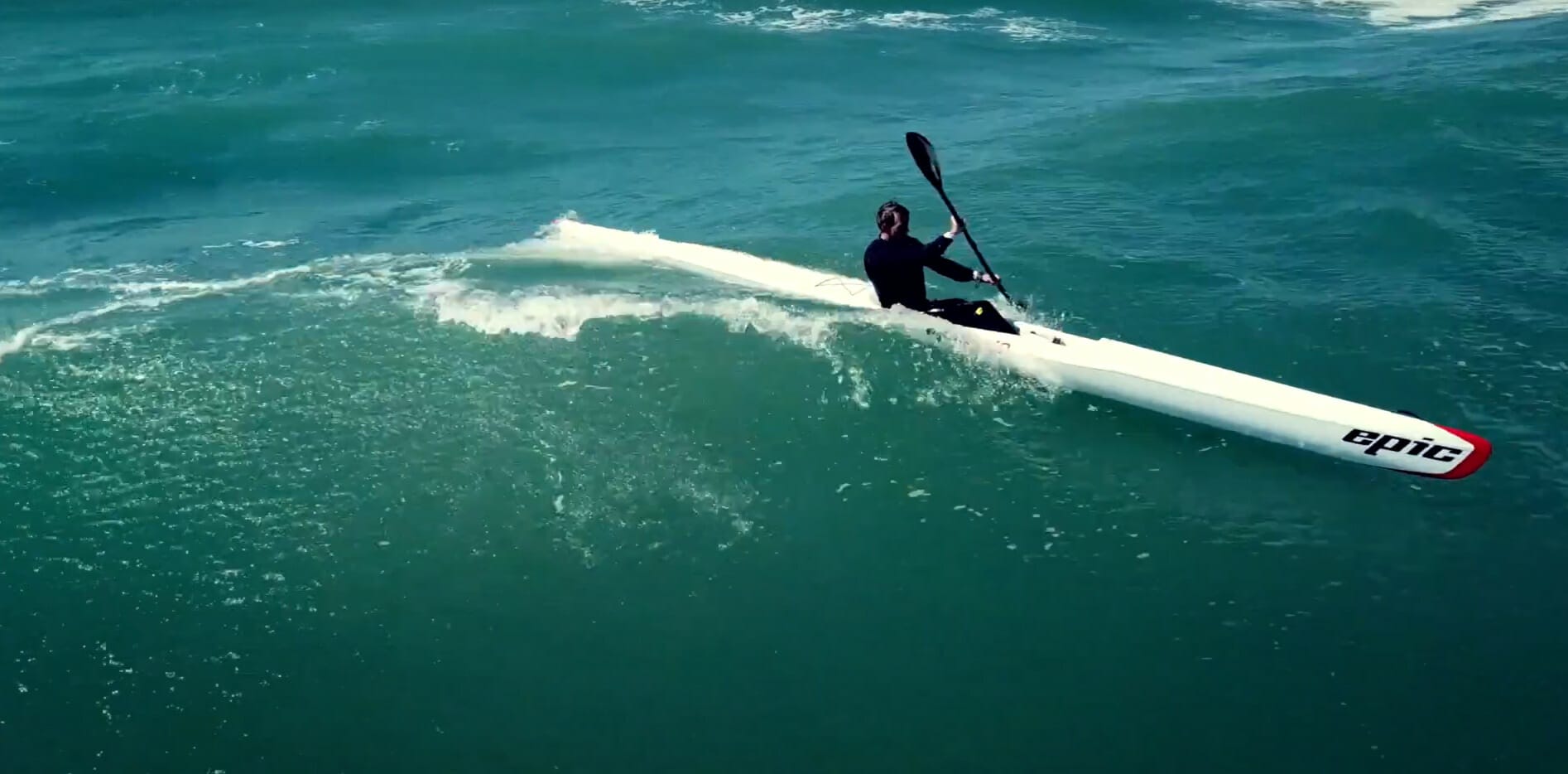 A man riding a surfski kayak on a wave in the ocean.